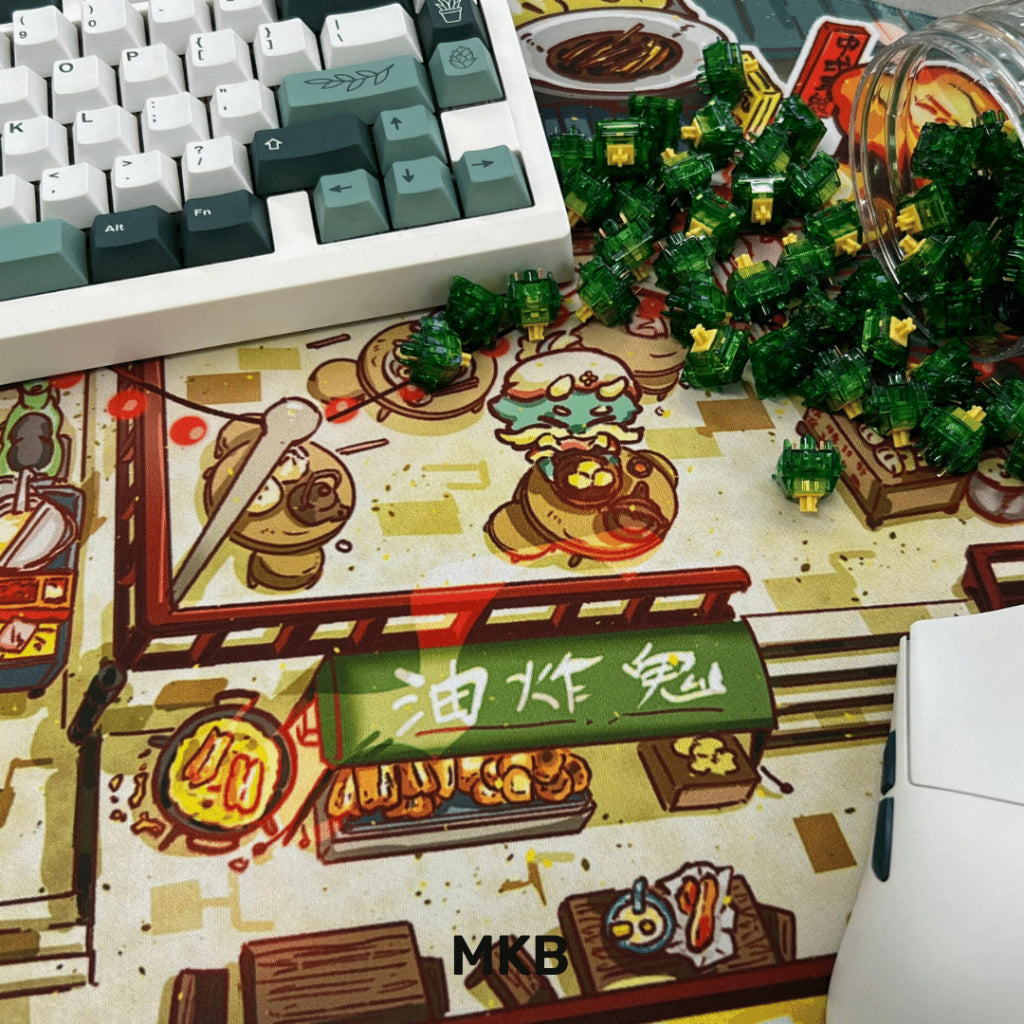 A flat lay of the MKB x FuwaFuwa deskmat with keyboards, keycaps, and accessories, highlighting its compatibility with various desk setups.